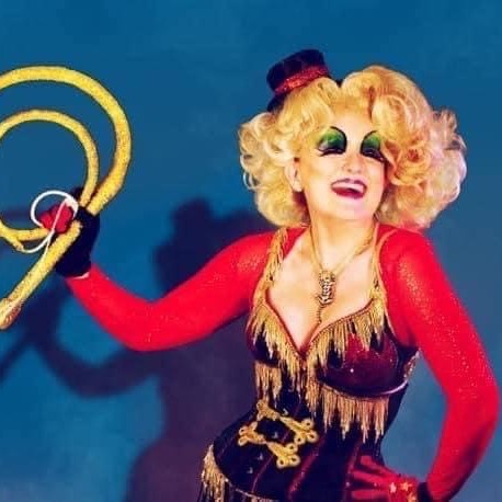 Cabaret performer Diva Hollywood is dressed as a sexy lion tamer, with curly blond wig, bright cabaret style make up and holding a whip