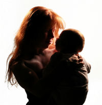 A woman holds a baby in her arms in front of a white background. 