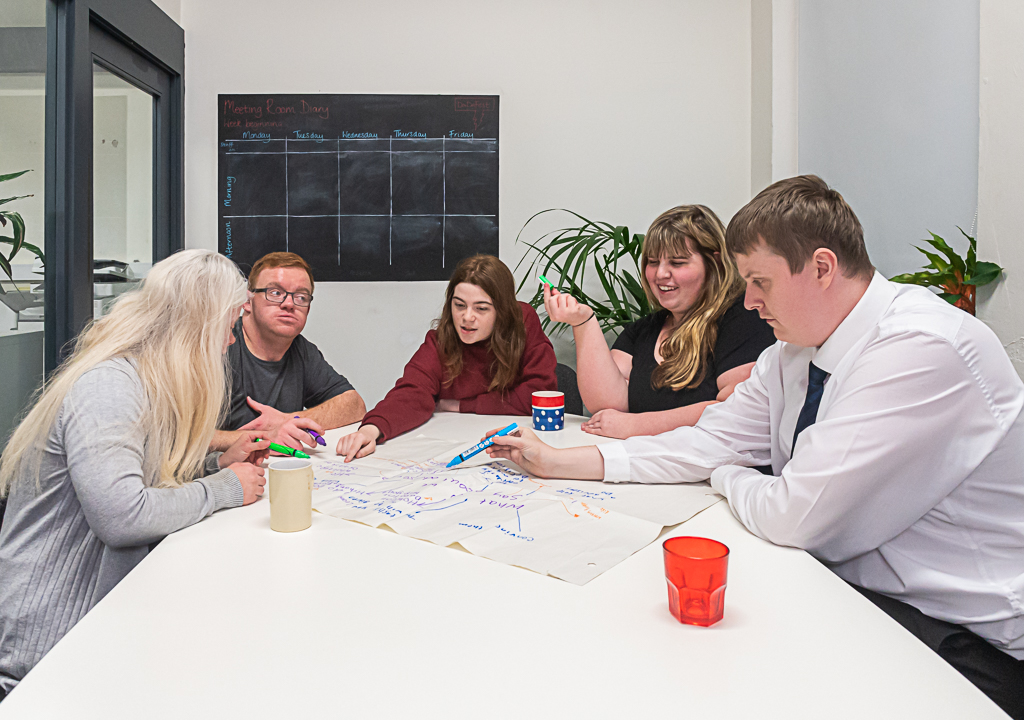 Five young people sat around a table looking a sheet of paper on which they are drawing a mind-map. 