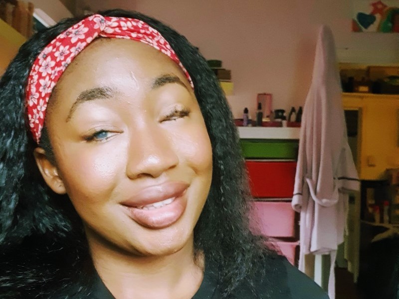 A black African-Nigerian woman with kinky/curly straight hair, wearing lip-gloss and smiling