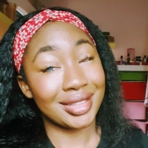 A black African-Nigerian woman with kinky/curly straight hair, wearing lip-gloss and smiling