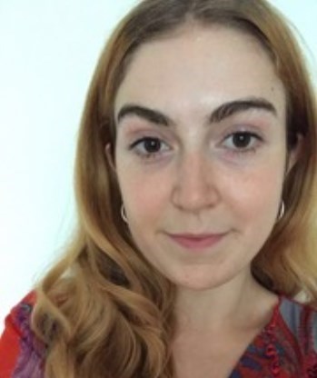 A white woman with shoulder-length ginger hair, brown eyes and thick brown eyebrows, wearing silver hoop earrings