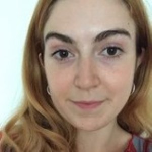 A white woman with shoulder-length ginger hair, brown eyes and thick brown eyebrows, wearing silver hoop earrings