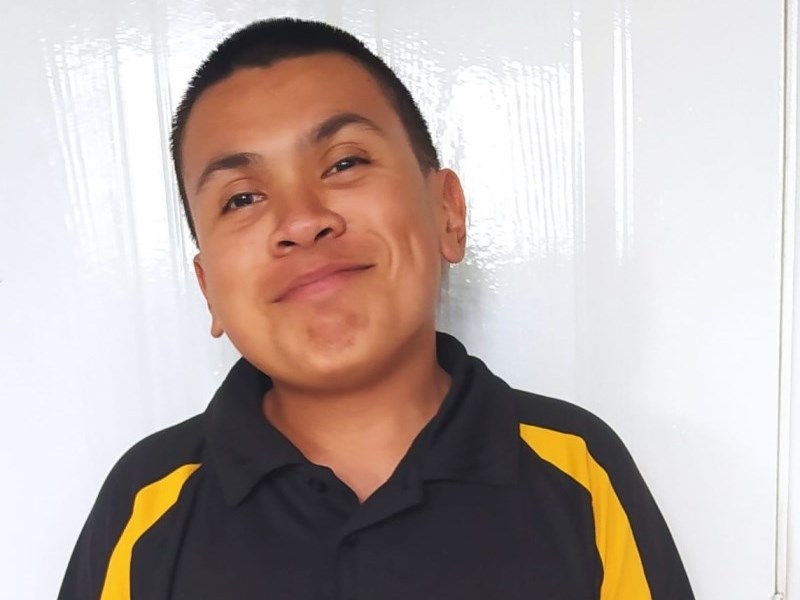 A mixed race East Asian and Bengali man with black hair wearing a black top that says 'Volunteer' alongside a logo for a Football museum