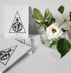 photograph of copies of the book Poem7 ona white surface next to a vase of flowers