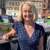 Gill is a blond woman wearing jeans and a blue top.