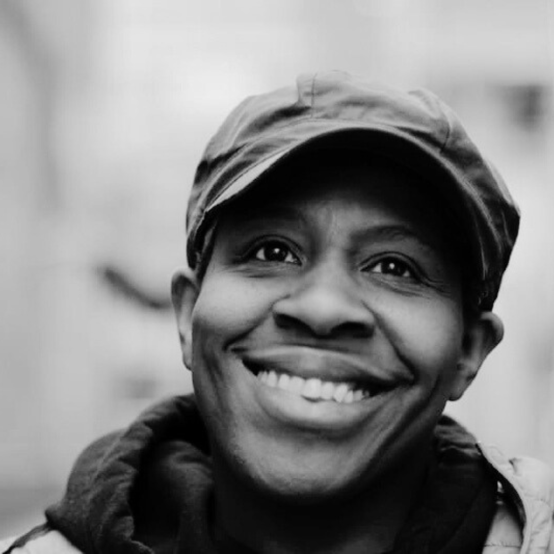 Black and white headshot of artist Ngozi Ugochukwu, a black woman with short hair, wearing a balck cap and smiling
