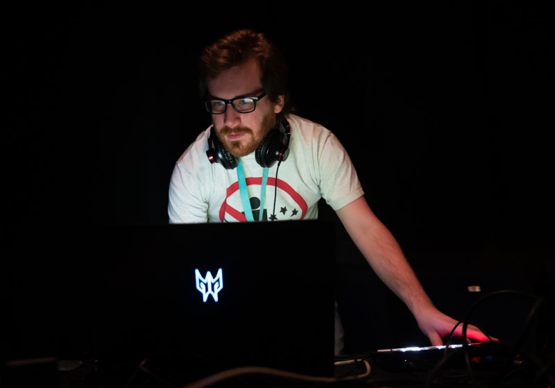 A person carrying out tech duties for a theatre production, their face illuminated by a laptop screen in what is otherwise a pitch black space. 