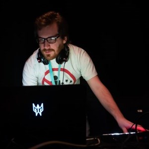 A person carrying out tech duties for a theatre production, their face illuminated by a laptop screen in what is otherwise a pitch black space. 