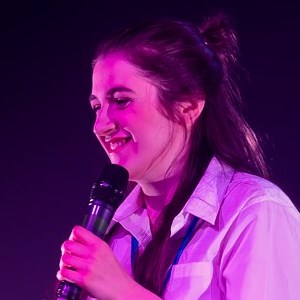 Performer onstage wearing a white shirt smiling at her phone