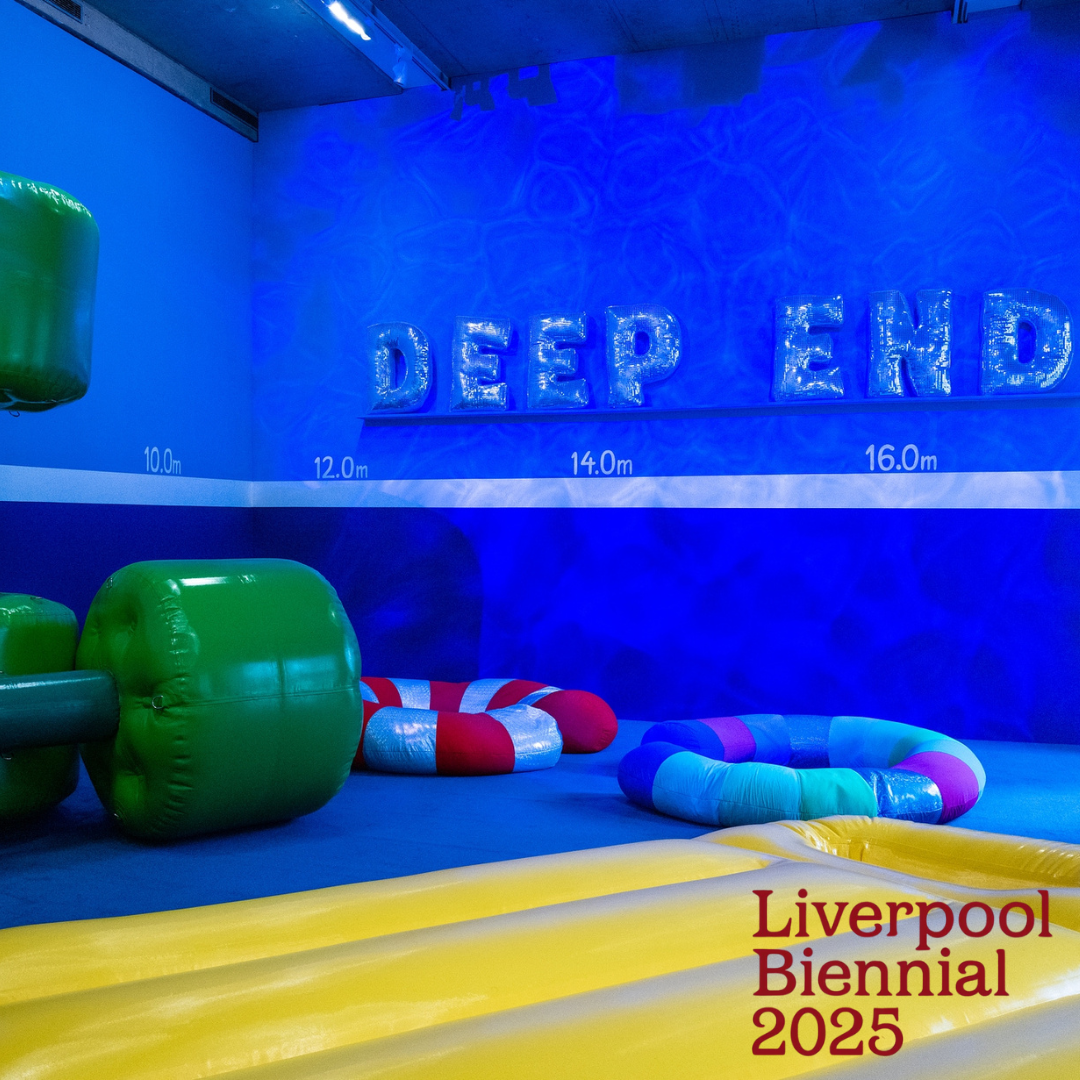 A bright blue wall carries inflated letters reading 'Deep End'. Beneath is a yellow inflatable lilo on the floor next to green inflatable dumbbells