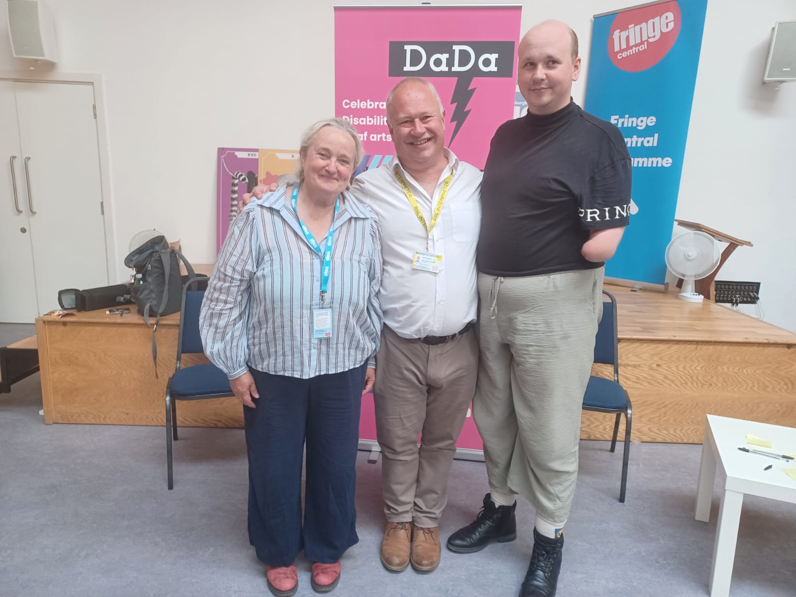 Denise and Ed from team DaDa stand with BSL Paul in front of DaDa pop up banner in Edinburgh 