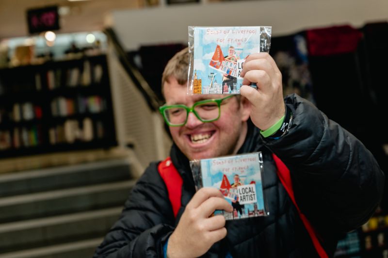 Album cover for Songs of Liverpool for Friends. Josh Henderson holds up illustration of Bluecoat and is surrounded by Liverpool Landmarks he has drawn