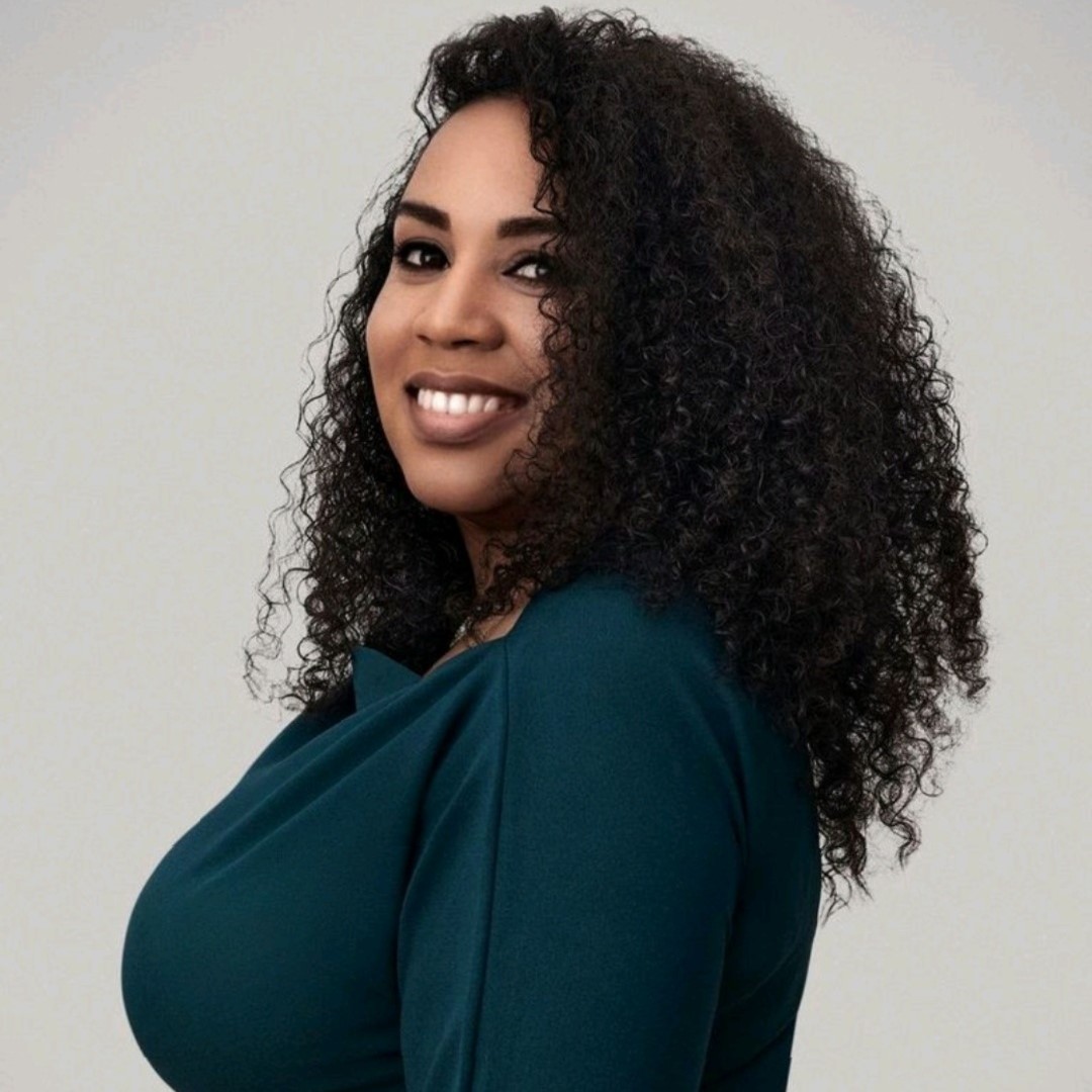 Image of black woman author Natalie Denny with long black hair, smiling wearing a long sleeve green top.