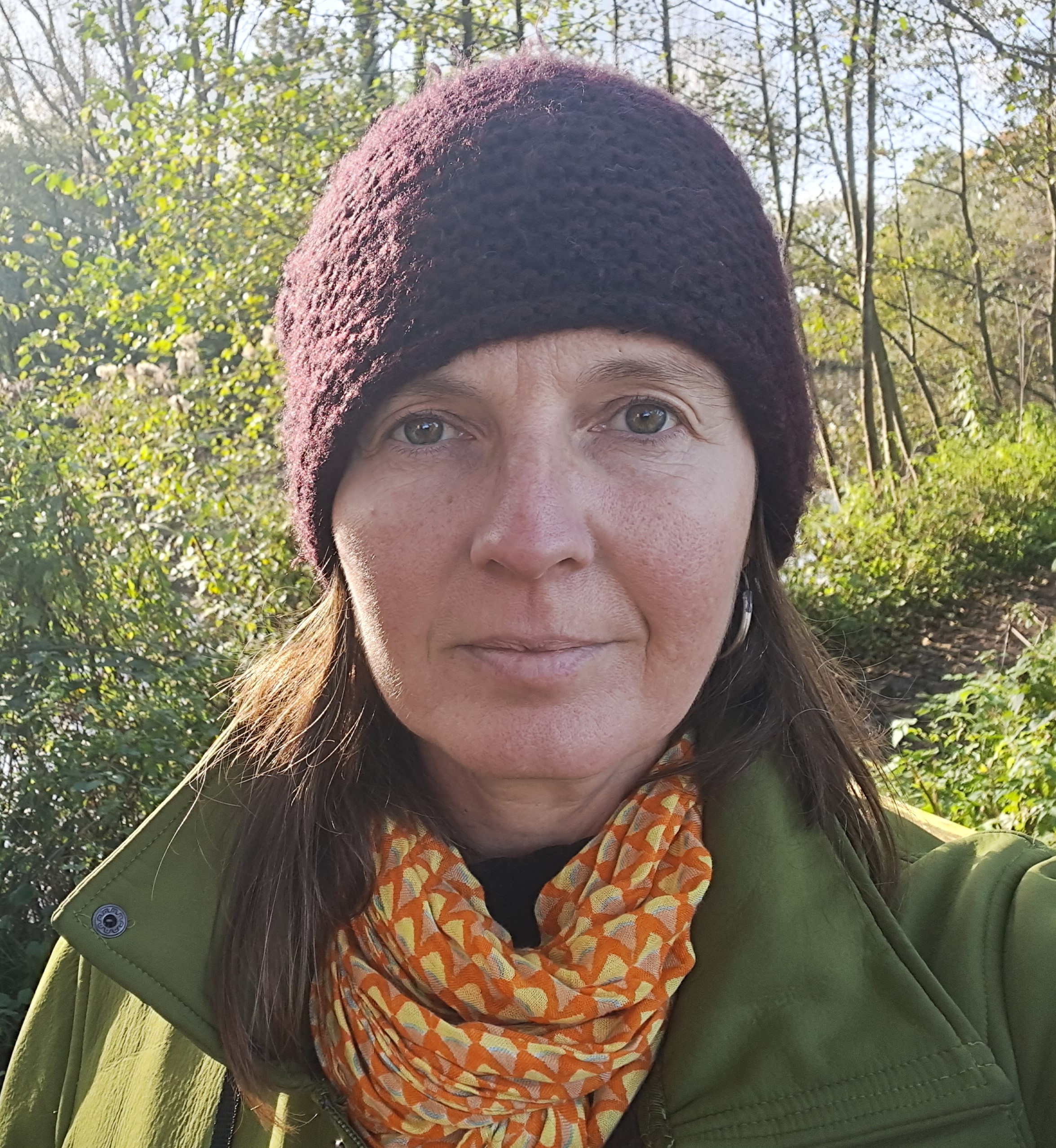 A photo of a woman wearing a wooley hat, green coat and mustard coloured scarf out in nature