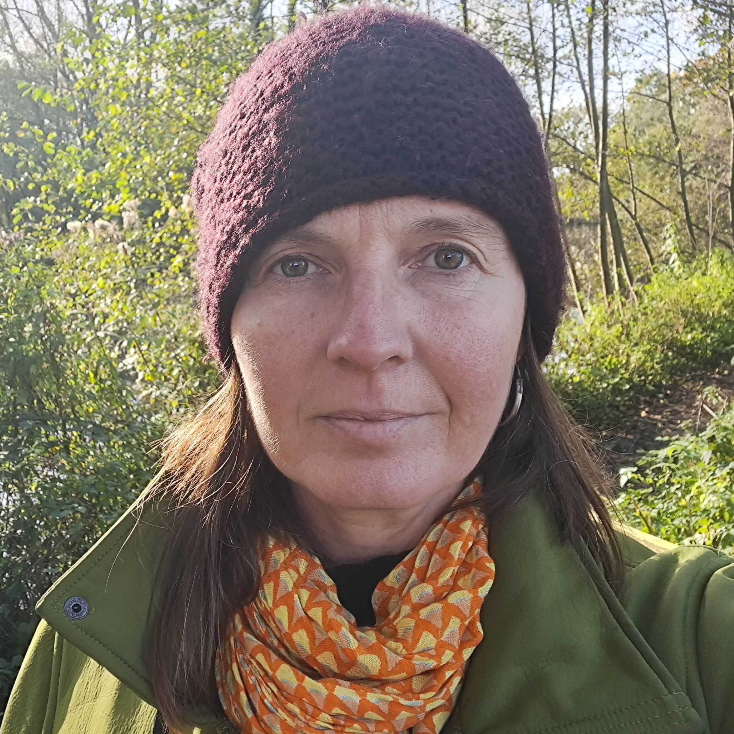 A photo of a woman wearing a wooley hat, green coat and mustard coloured scarf out in nature