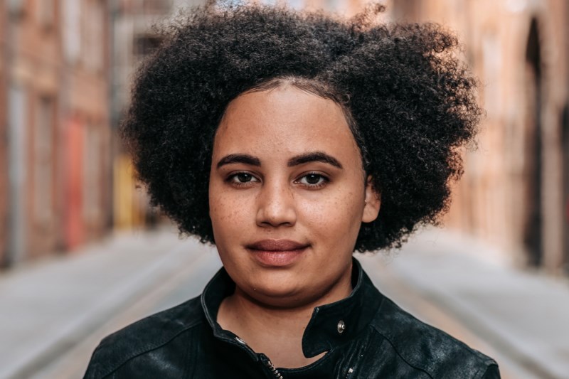 Woman of mixed Malawian and English heritage stood outside in a street smiling slightly