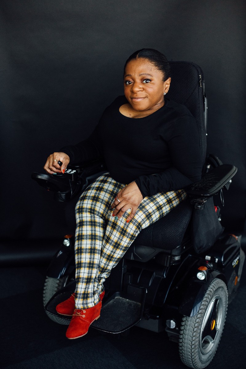 Monique sits in her wheelchair, smiling to camera