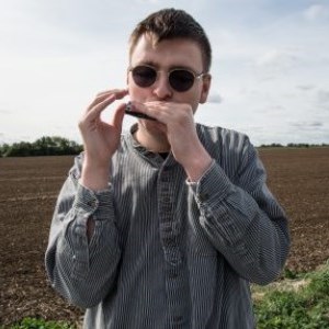 A young white man with brown hair playing a harmonica