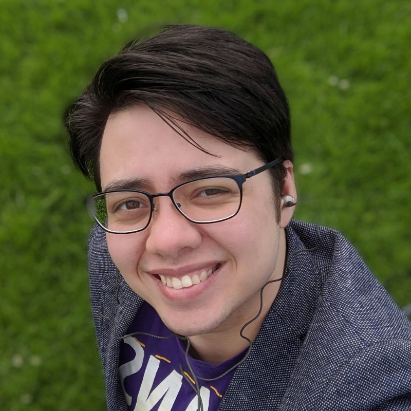 Image description: A photo of Julian against a grassy background; he is smiling at the camera. Julian is a mixed Chinese-white man in his twenties 
