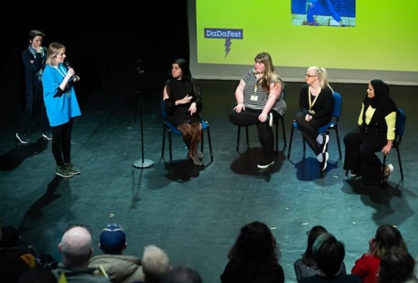 Six people onstage at a Q&A. One of them is stood up speaking into a microphone and others are listening intently. 