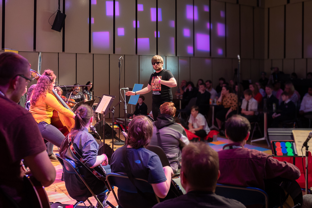 A concert space where a conductor, Ben Lunn, leads an orchestra of young musicians