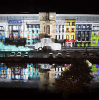 A photo of a projected image on a building of a street scene with a disability car driving along it