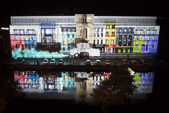 A photo of a projected image on a building of a street scene with a disability car driving along it