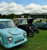 A photo of Simon standing in front of four Invalid Carriages of different ages parked in a field.