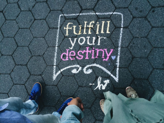 A photo of a chalk drawing on the ground which reads fulfil your destiny