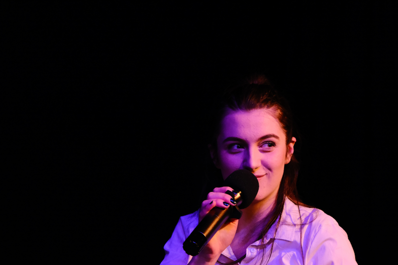 A performer in a dark space speaking into a microphone