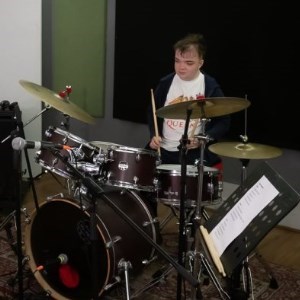 12-year old musician sat at a drum kit in a rehearsal studio
