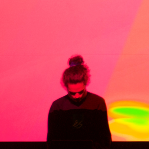 Musician with his long hair tied up in a top-know, looking downwards against a soft pink background