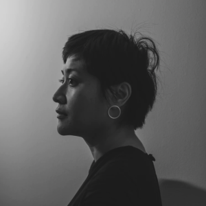 Black and white headshot of an Indonesian woman in profile with her dark hair in a pixie-cut hairstyle