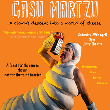 A man dressed as a maggot is lying on a bed of cheese pretending to lick a cheese grater.
