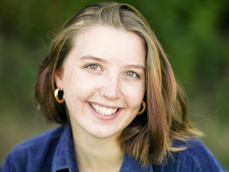 Rhiannon Jones gently smiles to camera in a close up. She uses a hearing aid. 