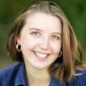 Rhiannon Jones gently smiles to camera in a close up. She uses a hearing aid. 