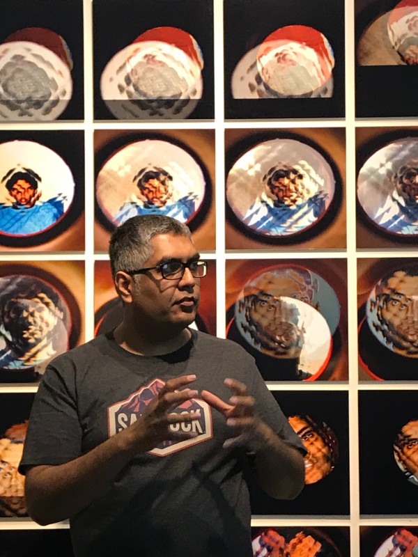 Ashokkumar_Mistry_stands in front of a wall of artworks