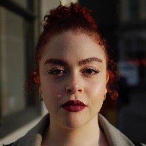 A woman with dark hair and red lipstick facing the camera 