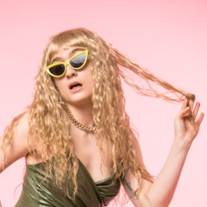 Artist Rosa Garland wears quirky yellow rimmed sunglasses and long curly haired blond wig.