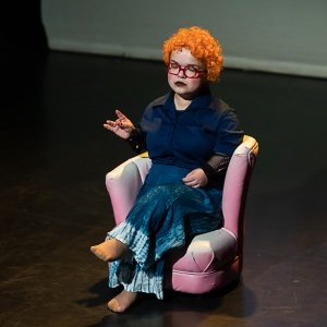 Tammy Reynolds sits on stage in a chair, eyes closed, her hair bright orange.